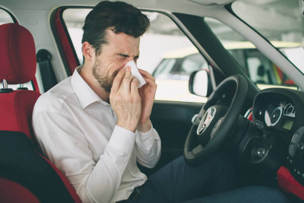 Homem no carro assoando o nariz com sinusite